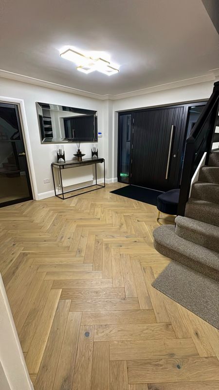 Oak herringbone flooring in an entrance hall with carpeted stairs