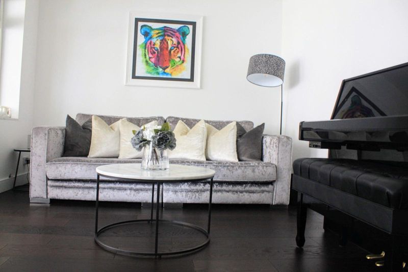 Bright lounge with grey velvet sofa, black piano and dark oak floor