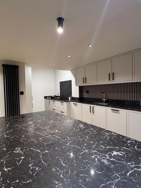 Black marble-effect worktop on a kitchen island with grey cabinets and a vertical radiator