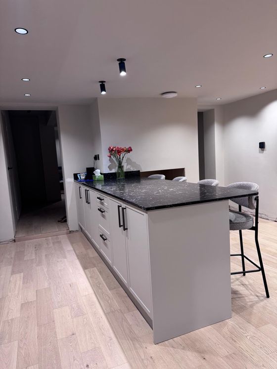 Long kitchen island with black granite worktop, bar stools and oak flooring