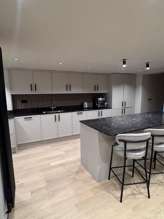 Grey kitchen with island, black worktops and spotlights over oak flooring